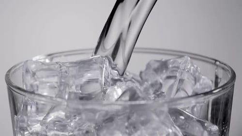 Close up slow motion water pouring into glass with ice cubes