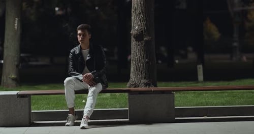 Jeune homme solitaire fumant, assis seul dans un parc nocturne vide,