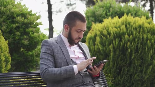 Man Uses Tablet in Park Wearing Suit