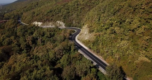 Luftaufnahme des Autos, das entlang der kurvenreichen Mountain Pass Road durch die Waldbäume fährt.
Herbst