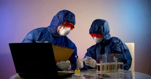 Personas con ropa protectora con capuchas, respiradores, gafas y guantes están sentadas en una mesa