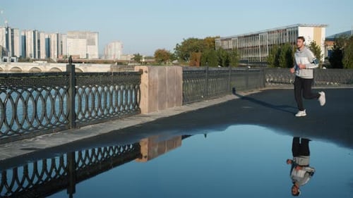 Slow Motion of Serious Sportsman in Headphones Jogging Outdoors in River Embankment