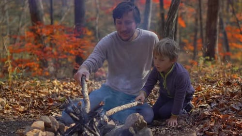 Young Man and His Little Son Sitting By a Bonfire in a Cold Autumn Forest. Autumn Vacation Concept