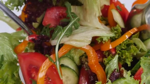 Frisches gemischtes Gemüse fällt in eine Salatschüssel, isoliert auf weiß. Zeitlupe.