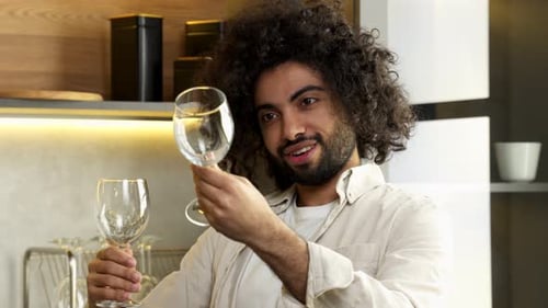 Cheerful Young Adult Inspecting Wine Glasses in Kitchen