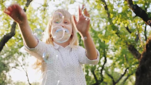 A Cheerful Blonde Girl Is Playing with Soap Bubbles. Carefree Happy Childhood Concept