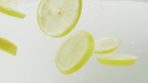 Lemon Slices Falls Into The Water In White Background. - close up