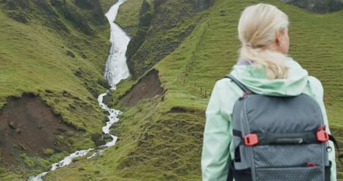 Touristin mit Rucksack genießt einen isländischen Wasserfall in der Nähe von Fjadrargljufur an der Südküste von