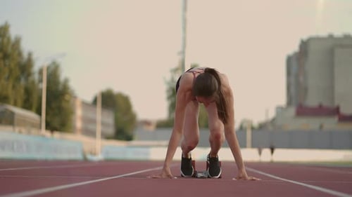 Eine junge Athletin grübelt sich auf und bereitet sich auf den Start eines Sprintrennen an einem sonnigen Tag vor
