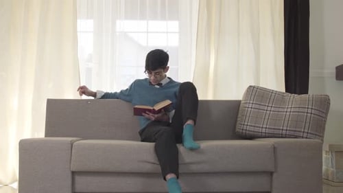 Portrait of Focused Caucasian Young Man Sitting on Sofa and Reading. Handsome University Student