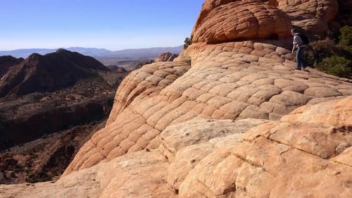 Woman hiking to the edge of a cliff to view valley below