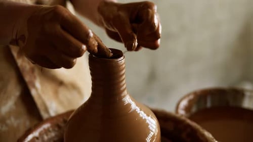 Une potière coupe l'excès d'argile sur le dessus du vase