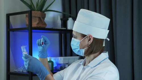 Arzt in Schutzkleidung, Gesichtsmaske und Handschuhen hält Reagenzglas mit Proben