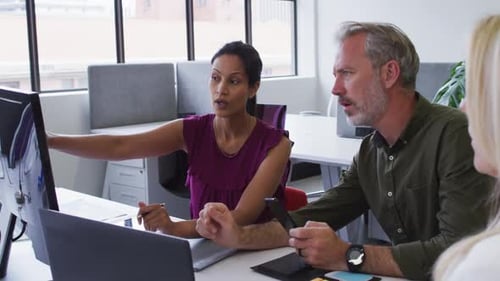 Diverse Geschäftskollegen sitzen am Schreibtisch am Computer und diskutieren im Büro