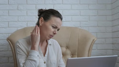 Woman Massaging Neck While Using Laptop