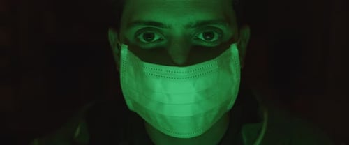 Portrait of a young man putting on a protective mask, green lighting.