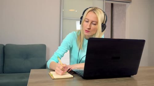 Woman working at a laptop while taking notes