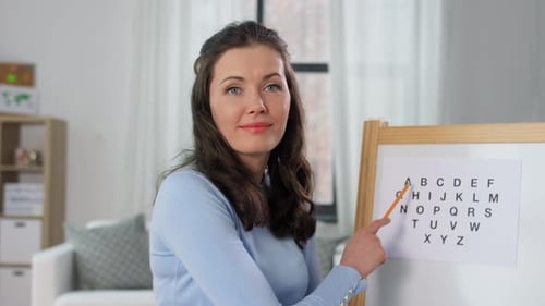 Woman Points to Alphabet on Whiteboard Indoors