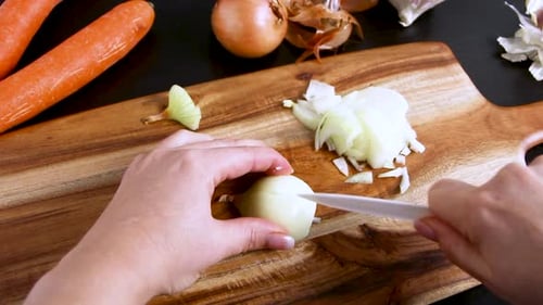 Woman's hands chopping fresh onion on a wooden board close up