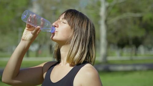 Woman Drinks Water in Park on Sunny Day