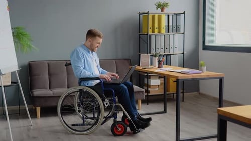 Disabled Person Freelancer is Working with Laptop Typing Sitting in Wheelchair at Office