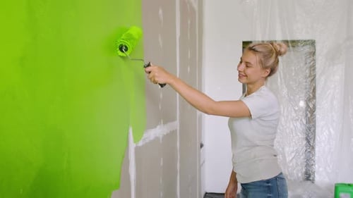 Une femme heureuse peint le mur en vert, un mec vient à elle et lui donne un cinq