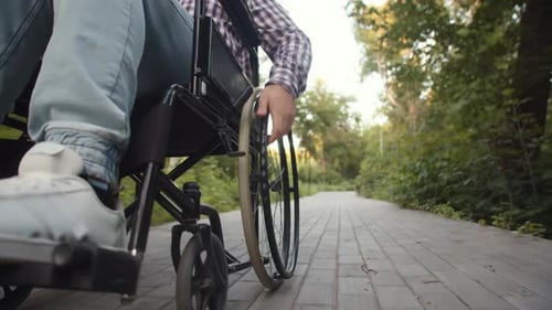 Man Propelling Wheelchair on Paved Path Outdoors