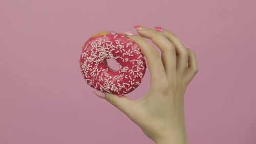 Hand Holding a Frosted Donut with Sprinkles
