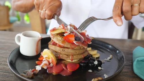Cutting Stack of Pancakes Topped with Fresh Fruit