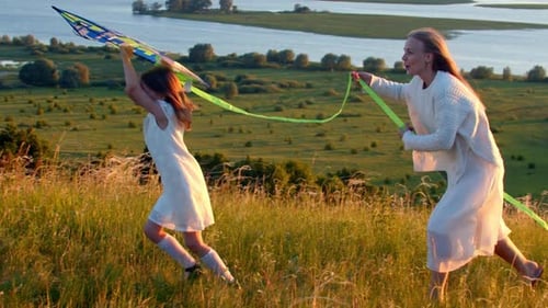 Young Mother with Her Daughter Running on the Field with the Kite at Sunset