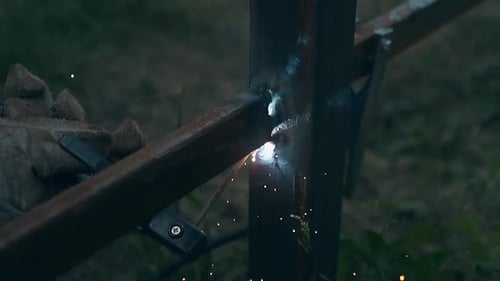 Un hombre de cerca en cámara lenta construye una cerca con una máquina de soldar