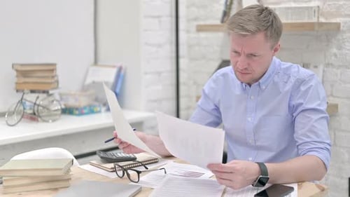 Man Reviews Documents at Desk in Office