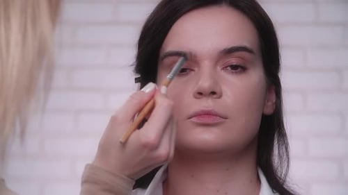 Makeup Artist Applies Eyeshadow on Female Eyes with White Brick Wall Behind
