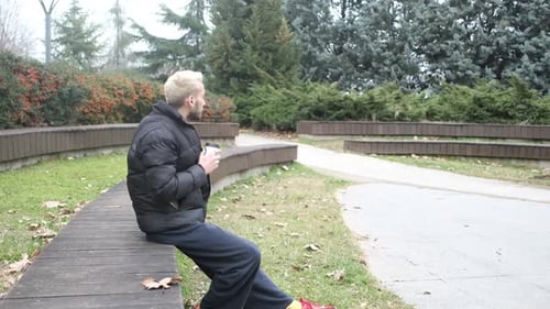 Man Drinks Coffee on Bench in a City Park