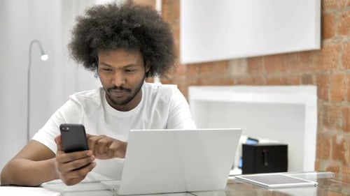 Young Adult Using Phone and Laptop at Desk
