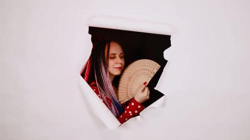 Mujer joven en vestido rojo con abanico en agujero de fondo blanco en estudio