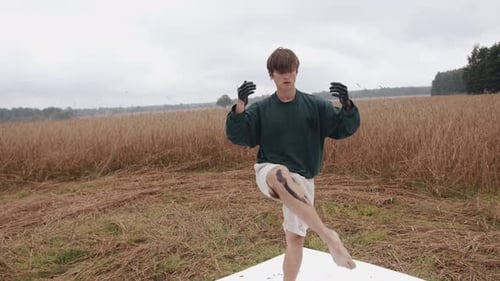 Un joven interpreta un baile alternativo en la naturaleza y con las manos sumergidas en hojas de pintura negra