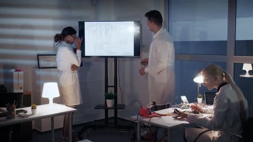 Intelligentes Team von Elektronikentwicklern diskutiert im Labor etwas auf einem großen Fernsehbildschirm