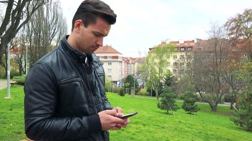 Young Handsome Man Stands, Works on Mobile Phone and Looks Around
