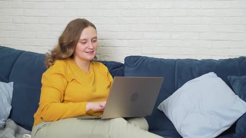 Woman Working on Laptop While Relaxing on Couch