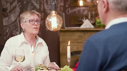 Mature Woman Talking at Candlelit Restaurant Table