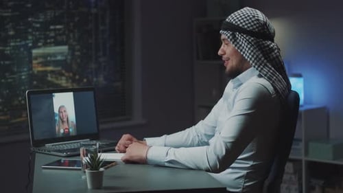Profile View of Young Arabic Man Making Video Call on Computer with Blonde Woman From Seaside