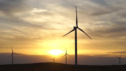 Motion the Blades of a Large Wind Turbine in a Field Against a Background of Orange Sunset on the