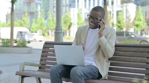 Annoyed Man Talking on Phone While Working on Laptop