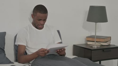 Man Reading Documents in Bed Reacts Positively