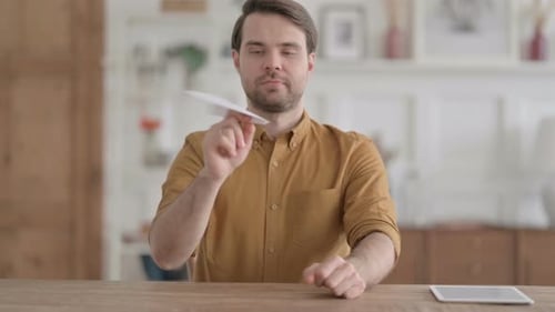 Young Man Making Paper Plane while Sitting in Office