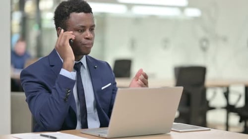 Serious Young Adult Talking on Smartphone at Desk