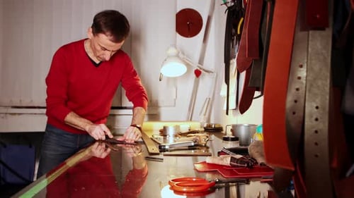 Leather Workshop a Man schneidet mit einem scharfen Werkzeug die Kanten des Lederstücks