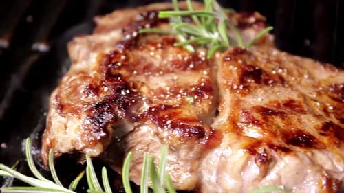 Grilling beaf steak. Cooking and pouring pepper on meat. Delicious food preparation.