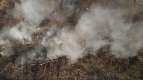 Aerial top-down trucking shot over the wildfire in the suburban area covered by a thick smoke